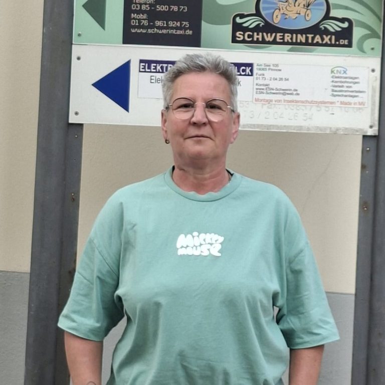 Uta Laudahn - Geschäftsführerin Frau mit grauen Haaren in mintgrüner T-Shirt steht vor einem Informationsschild.