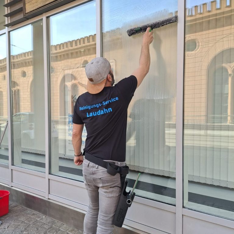 Fensterreinigung Ein Mann reinigt Fenster mit einem Wischgerät an einem modernen Gebäude.